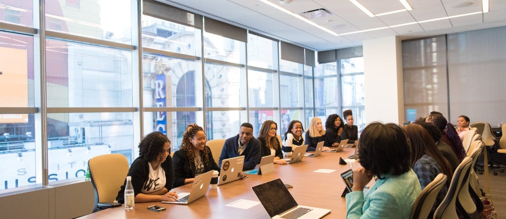 Diverse group of professionals collaborating around a conference table with laptops in a modern meeting room with large windows