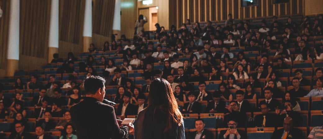 Speakers presenting to a large audience in a lecture hall or auditorium, depicting an academic conference or educational event